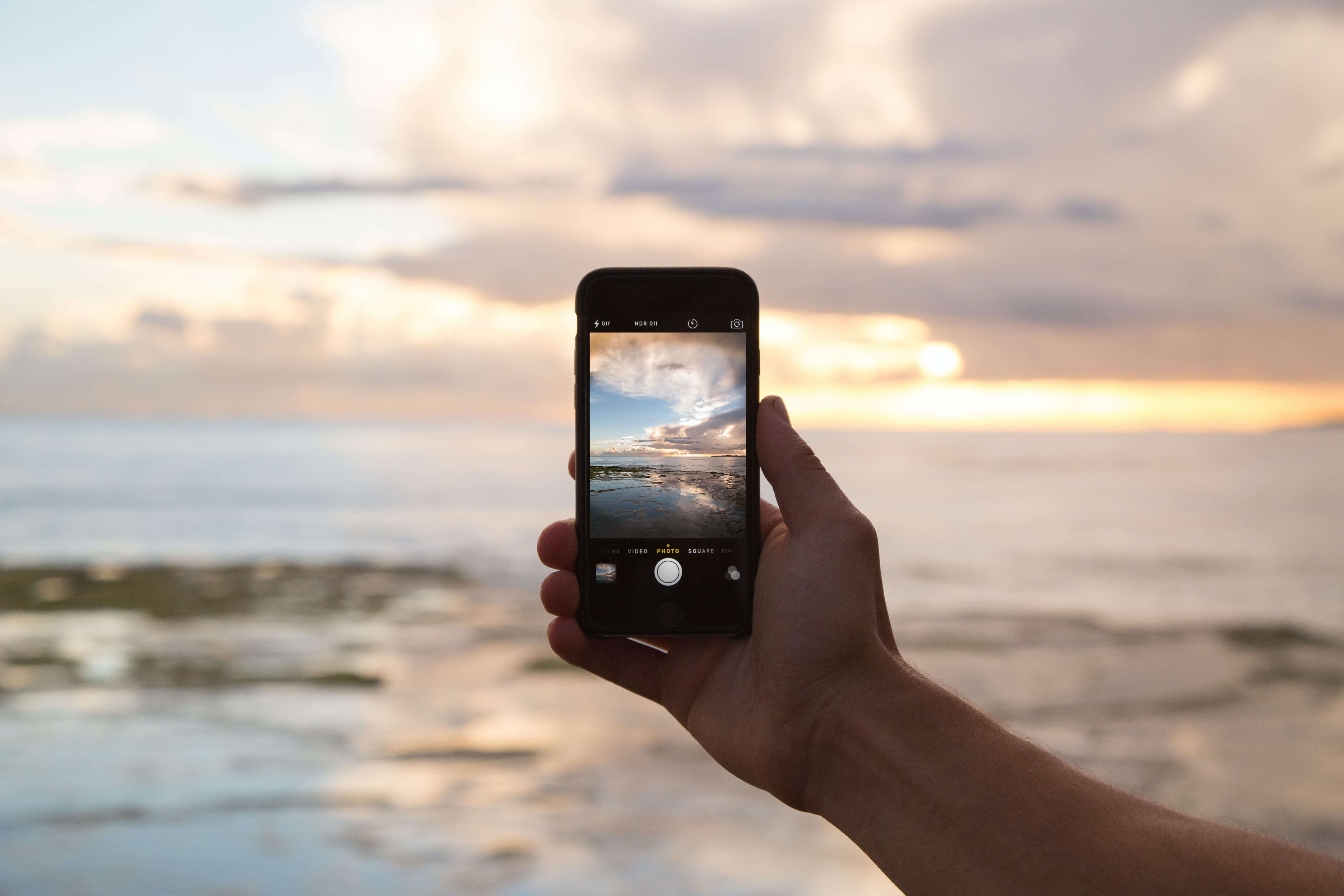 Man holding iPhone showing sunset over ocean